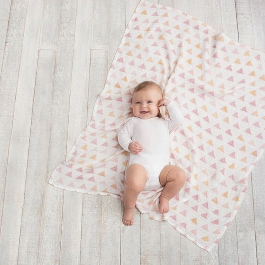 Happy baby lying on an Eclectic Aden + Anais metallic primrose birch bamboo muslin swaddle blanket