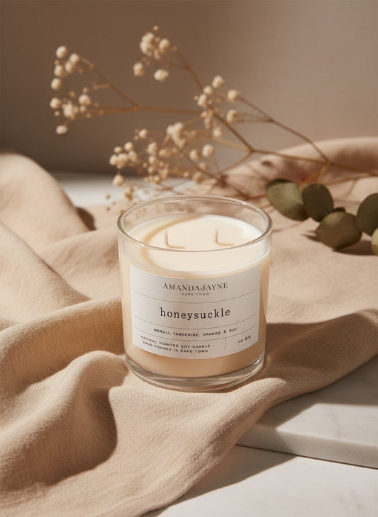 Eclectic Amanda Jayne Honeysuckle double wick soy candle in a glass jar on beige fabric with dried flowers.