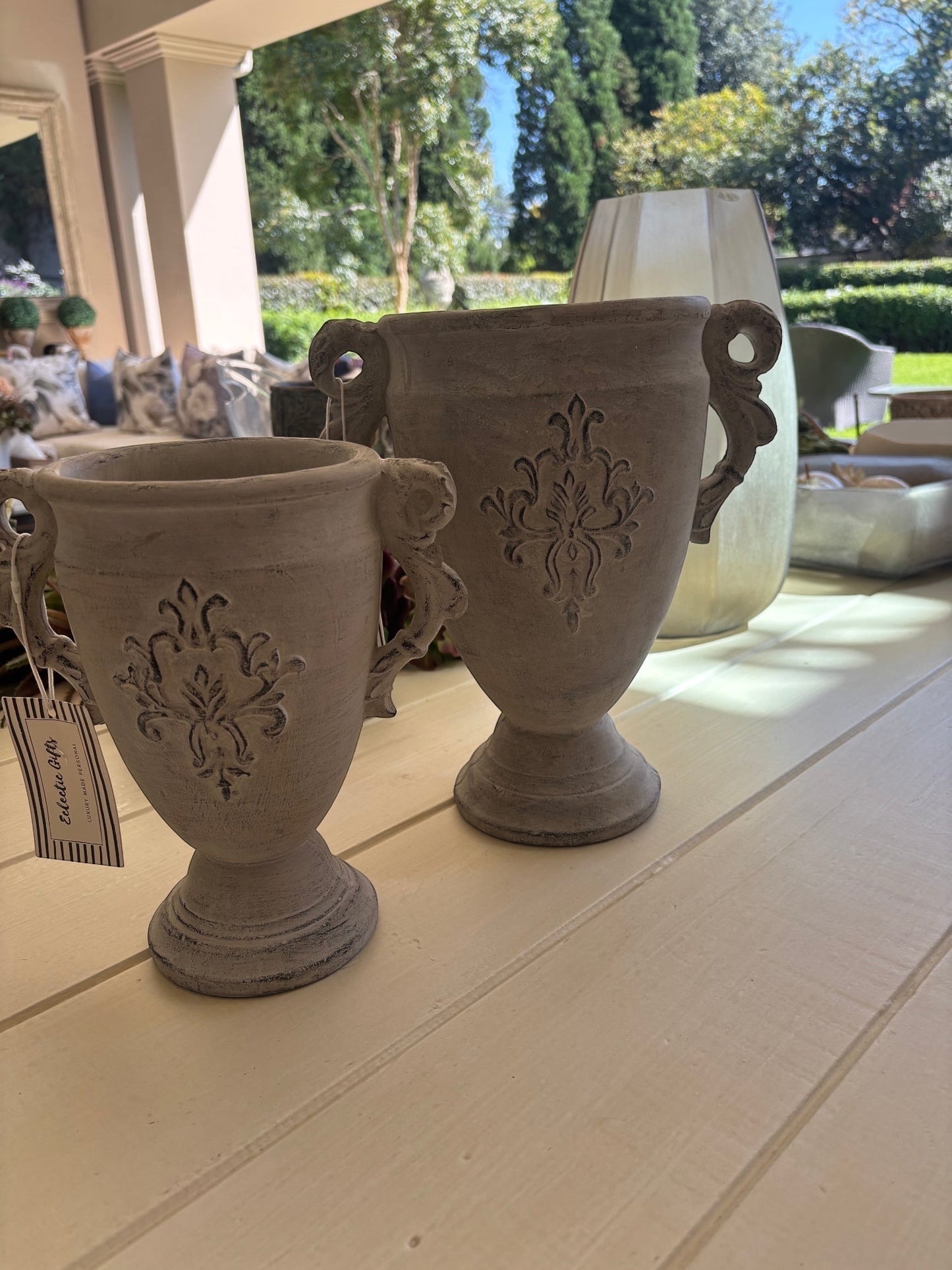 Eclectic antique cement trophy vase planters with ornate handles and weathered finish on a white table