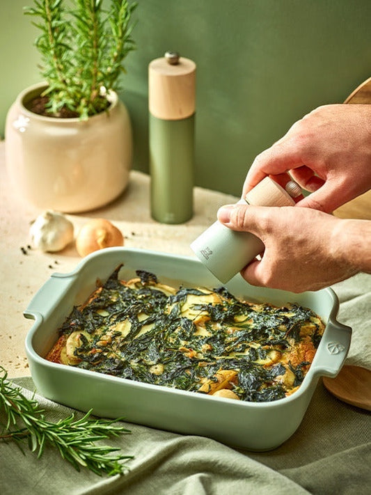 Eclectic Appolia rectangular ceramic oven dish in sage green filled with a baked vegetable gratin on a kitchen table.