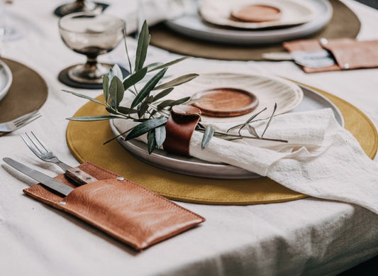 Eclectic ASA Selection mustard vegan leather placemat on a dining table with a napkin, cutlery, and olive branch.
