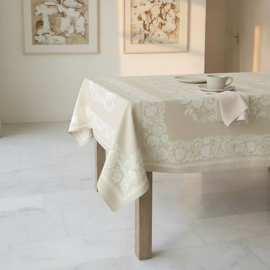 Eclectic beige linen-look tablecloth with an intricate white floral border draped over a dining table.