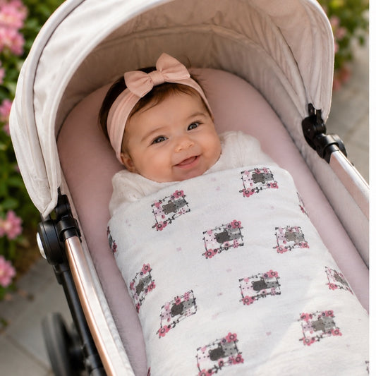 Eclectic Biddykins white cotton flannel baby blanket with kitty print, covering a smiling baby in a pram.