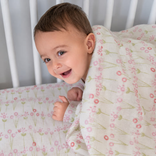 Eclectic baby smiling in a white crib under a soft cotton flannel blanket with a pink and green floral bloom print.