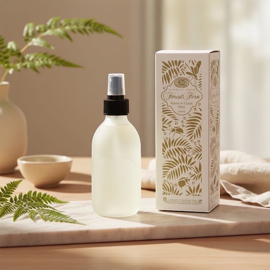 Eclectic Forest Fern room and linen mist in a frosted glass bottle next to its decorative box on a marble surface.