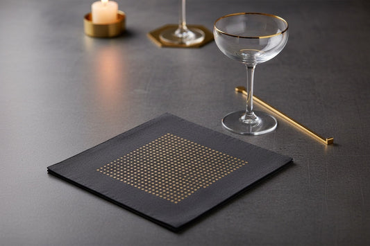 Eclectic Françoise Paviot black airlaid cocktail napkin with gold dot pattern on a dark table setting