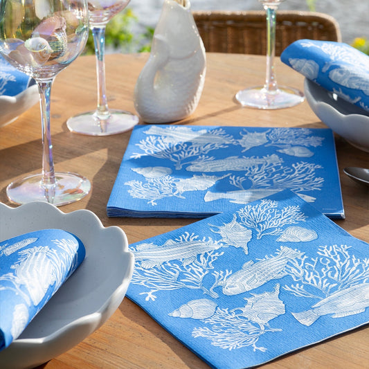 Eclectic Françoise Paviot Fonds Marin blue airlaid dinner napkins with white fish and coral motifs on a wooden table.