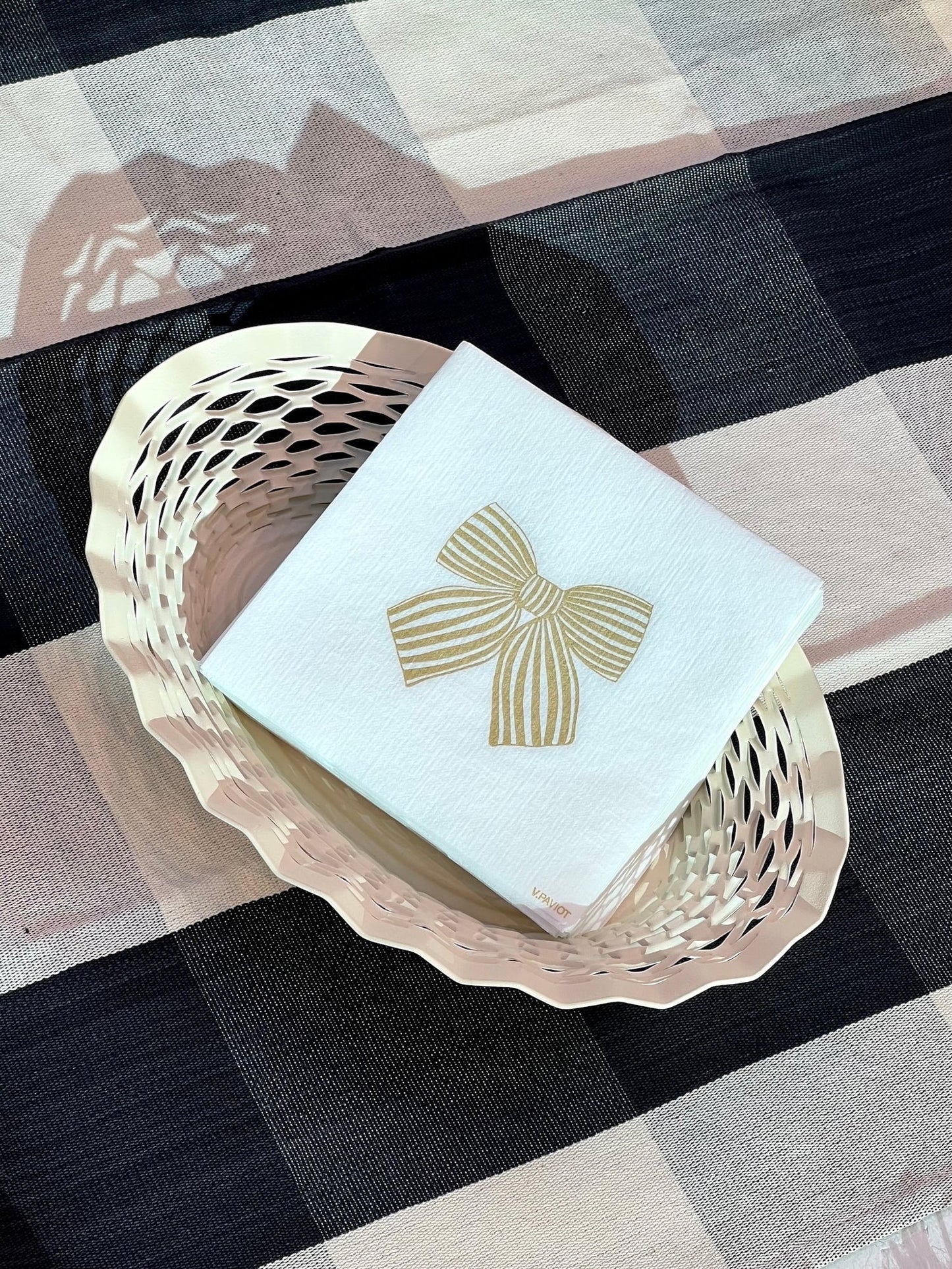 Eclectic Françoise Paviot Noeud Or cocktail napkin with a gold bow design in a decorative basket on a plaid cloth.