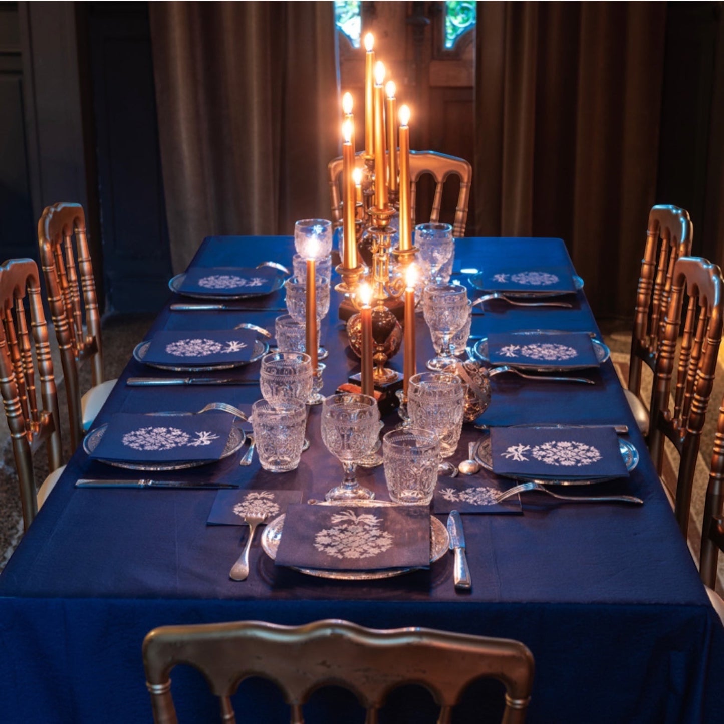 Eclectic Françoise Paviot Éclat du Soir midnight blue and silver dinner napkins set on an elegant candlelit table.