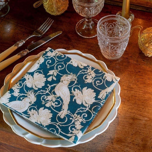 Eclectic Françoise Paviot petrol blue airlaid dinner napkin with ivory parakeet and floral arabesque design on a plate.