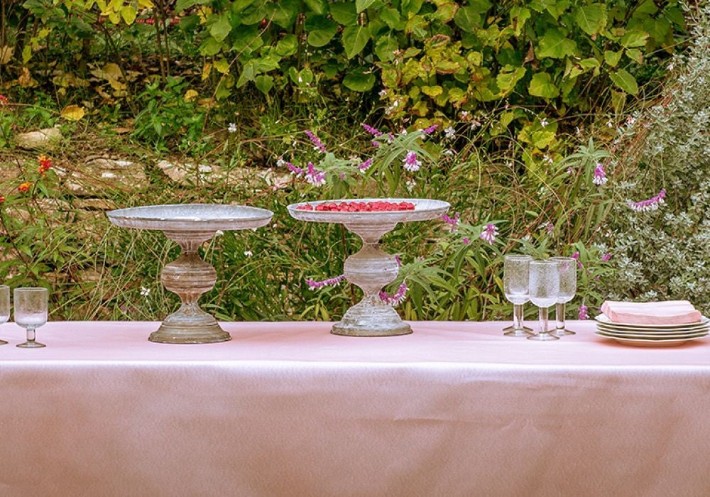 Eclectic Françoise Paviot rose dinner napkins stacked on a table with cake stands in a garden setting