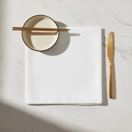 Eclectic Françoise Paviot white airlaid dinner napkin on a marble table with gold cutlery and a small bowl