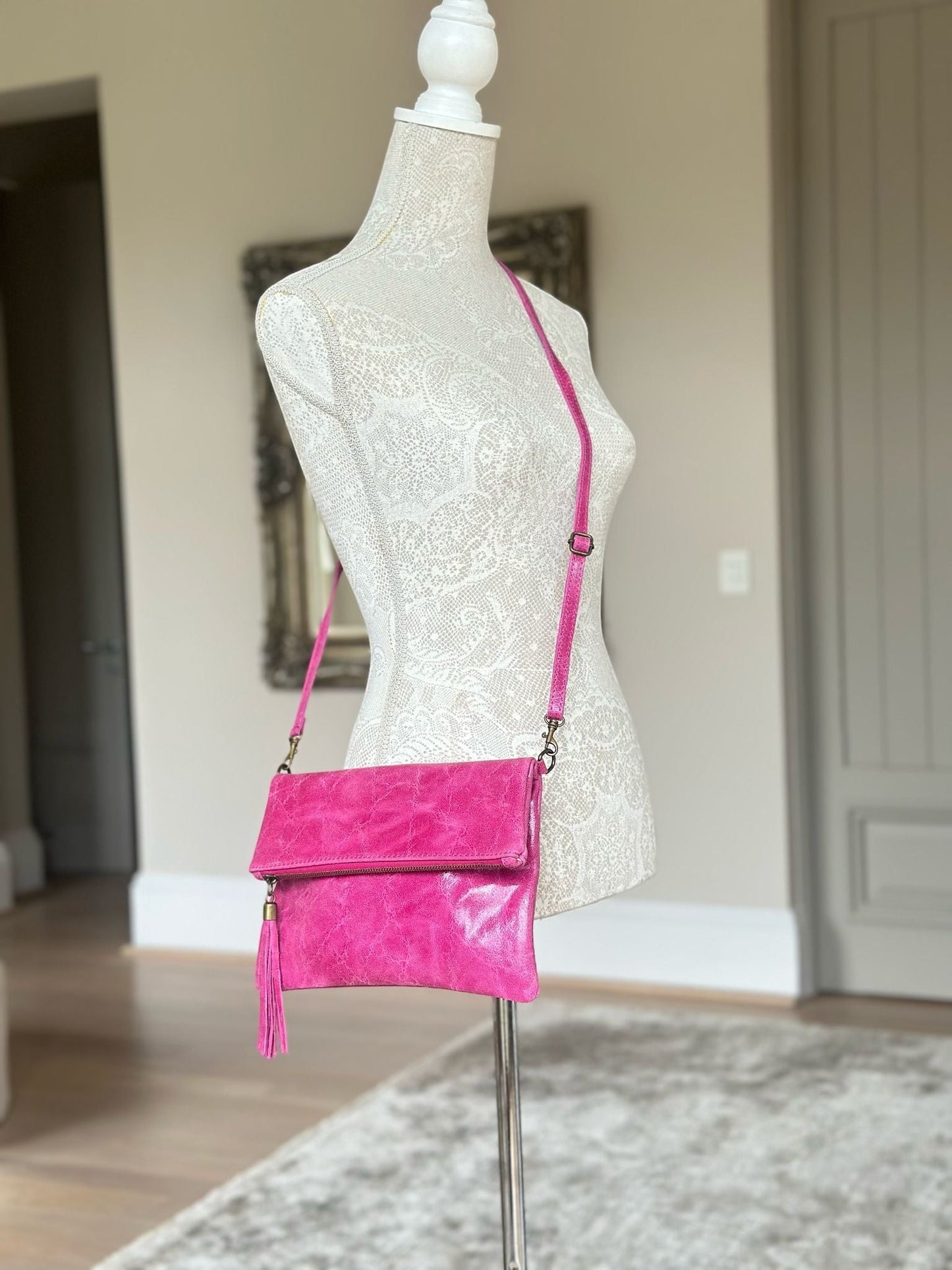 Eclectic fuchsia leather foldover clutch with a tassel and adjustable crossbody strap displayed on a mannequin.