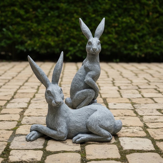 Eclectic Humphrey & Harriet cement hare garden sculptures in a weathered stone grey finish on a paved patio.