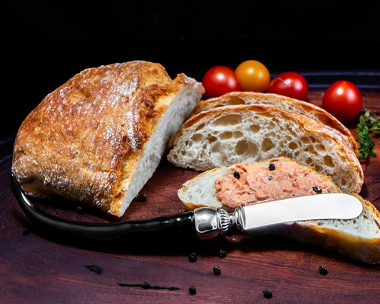 Eclectic Impondo Zulu pâté knife with a polished black horn-style handle and stainless steel blade on a bread board.