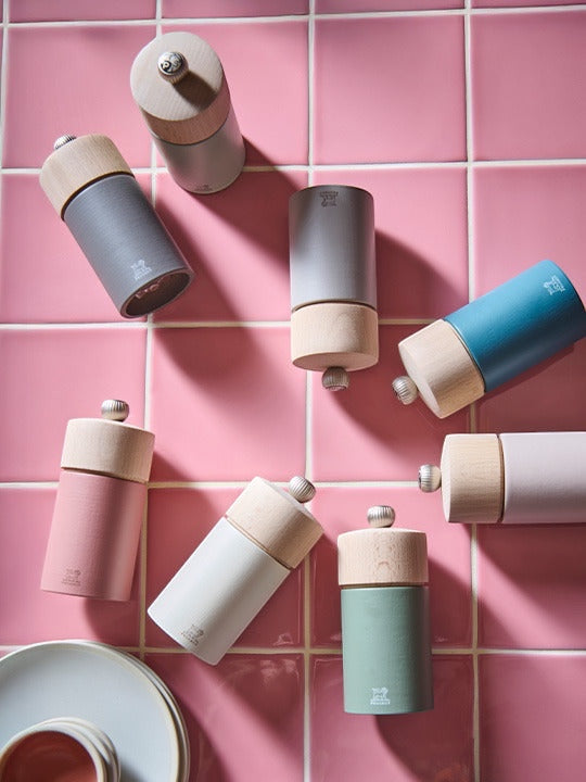 Eclectic Peugeot Boreal collection pepper and salt mills in various pastel colours on a pink tiled surface.