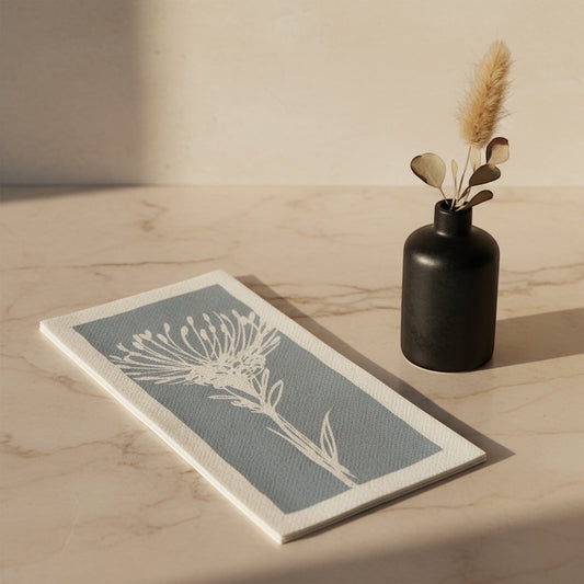 Eclectic Pincushion blue disposable airlaid napkin with a botanical protea print on a marble surface with a vase.