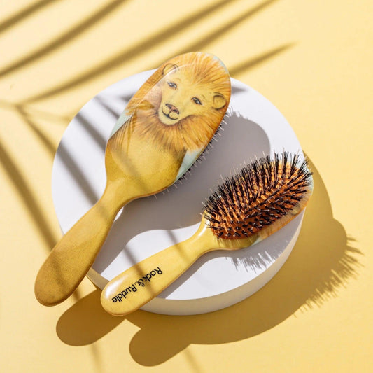 Eclectic Rock & Ruddle Lion baby hairbrush with natural boar bristles and a golden lion illustration on a yellow base.