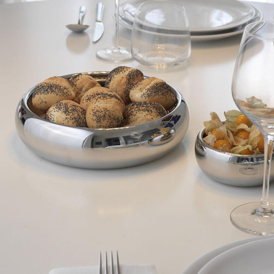 Eclectic Sambonet Sphera stainless steel serving bowl filled with bread rolls on a modern white dining table