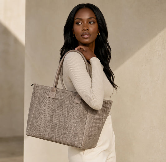 Model carrying a taupe snake-print suede shopper bag from Eclectic, featuring top handles and a structured design.