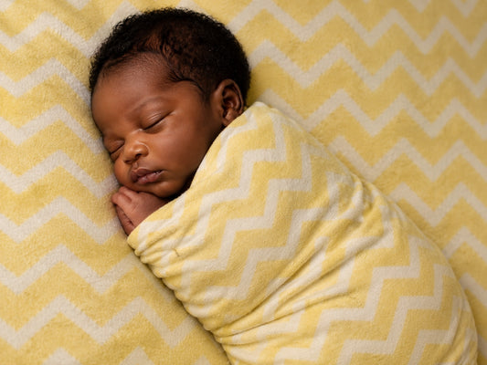 A sleeping newborn wrapped in an Eclectic yellow and white chevron cotton flannel blanket.