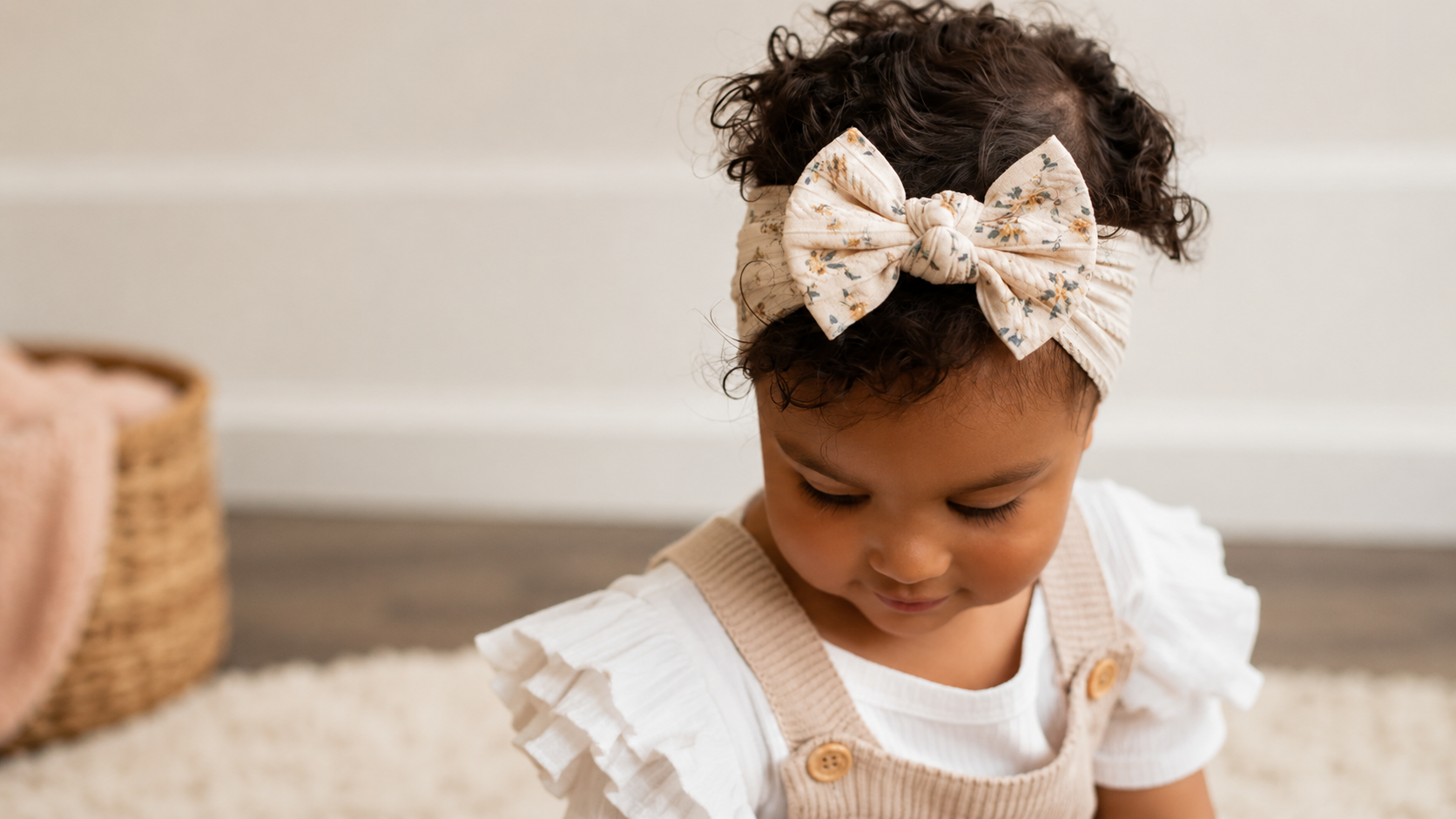 Child wearing a floral bow headband in a soft nursery setting.