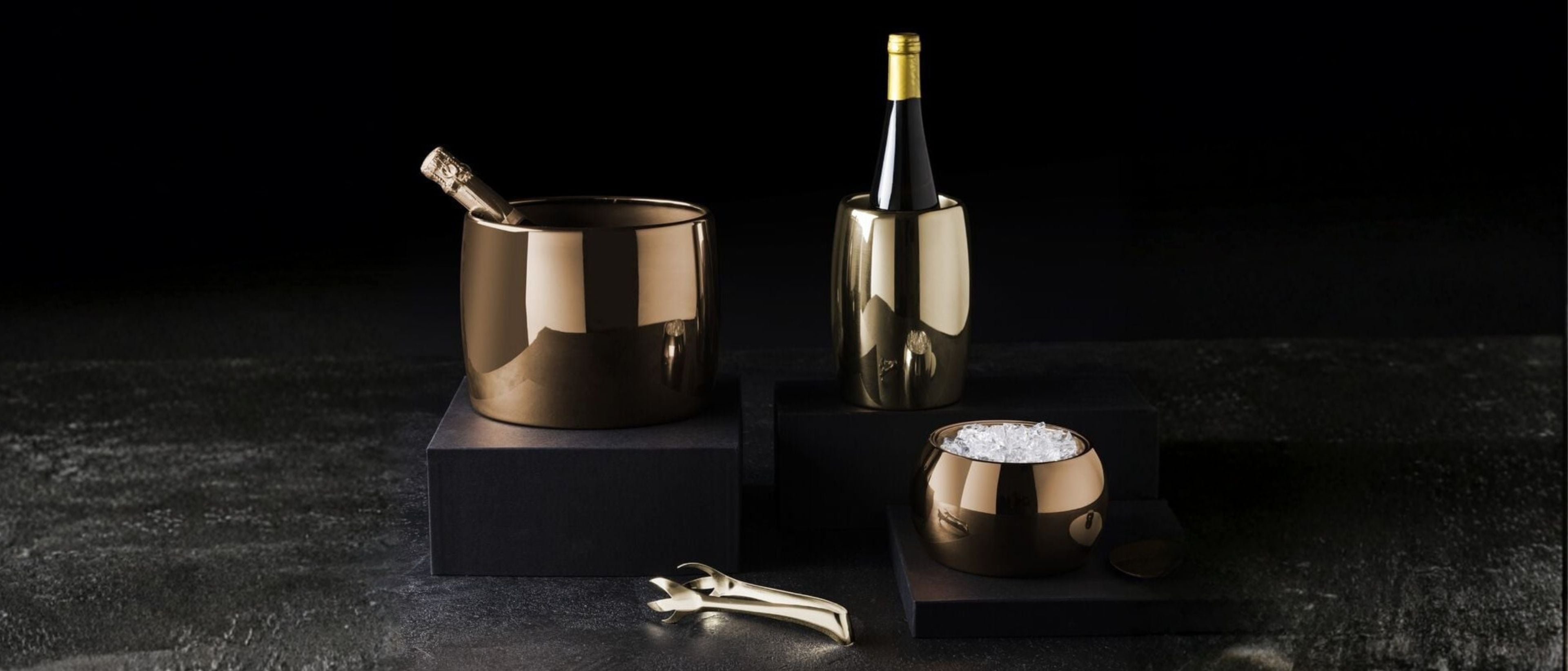 Metallic ice buckets and wine coolers with a bottle and ice tongs on a dark surface.