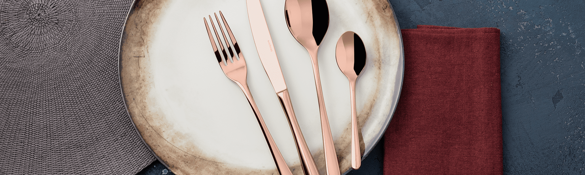 Rose gold cutlery set arranged on a ceramic plate with linen napkins.