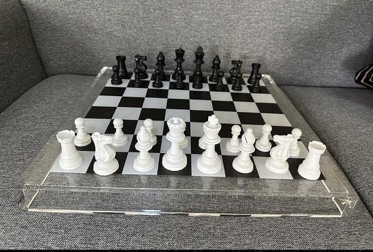 Eclectic 56cm square acrylic chess board with modern black and white pieces set on a grey sofa
