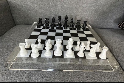 Eclectic 56cm square acrylic chess board with modern black and white pieces set on a grey sofa