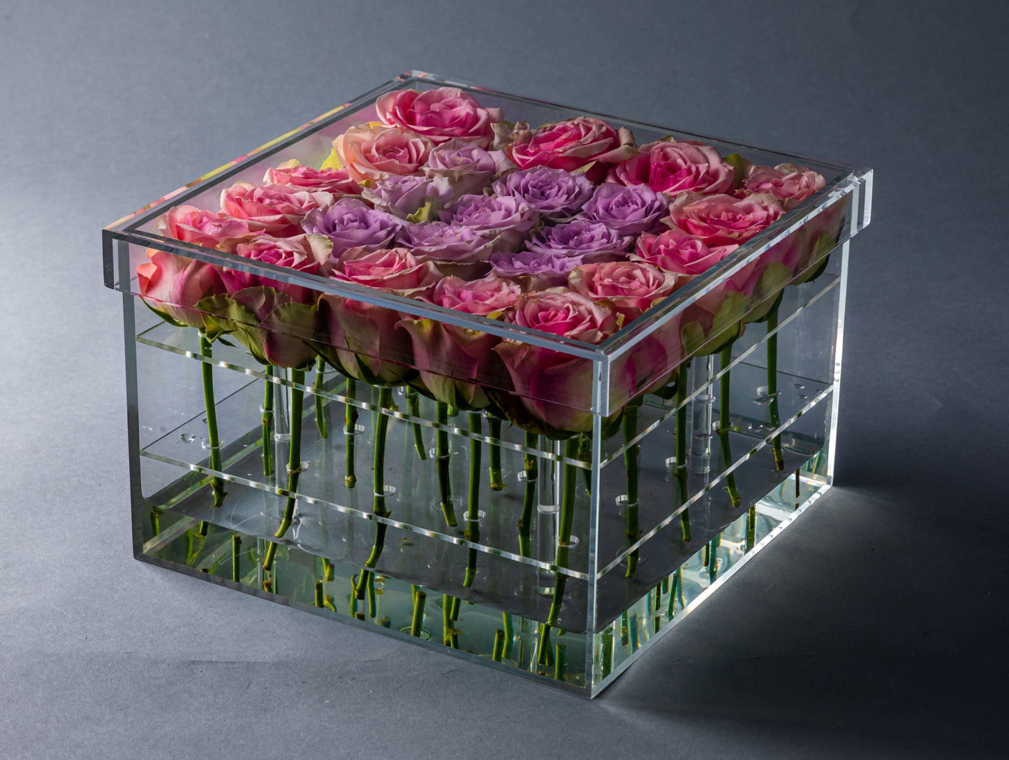Eclectic square acrylic box filled with pink and purple roses arranged in a clear display case