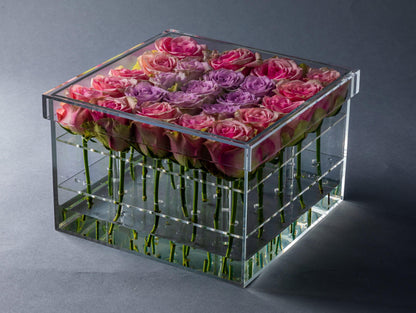 Eclectic square acrylic box filled with pink and purple roses arranged in a clear display case