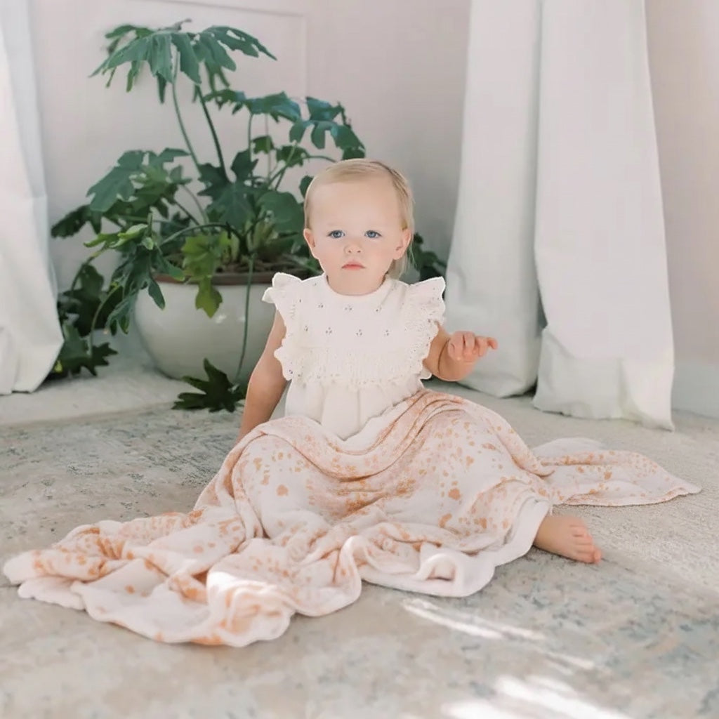 Eclectic Aden + Anais Metallic Primrose dream blanket draped over a toddler sitting on a nursery floor.