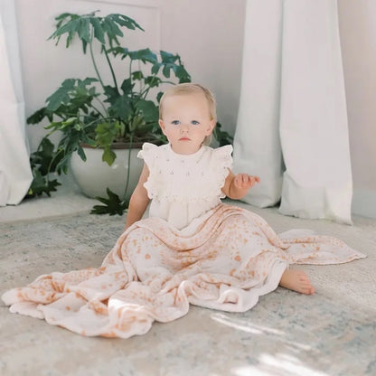Eclectic Aden + Anais Metallic Primrose dream blanket draped over a toddler sitting on a nursery floor.