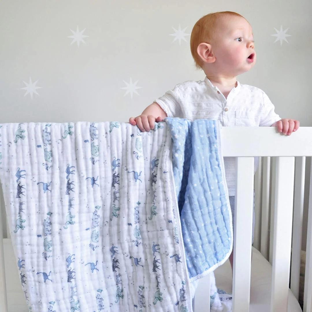 Eclectic Aden + Anais Rising Star muslin dream blanket draped over a white cot with a toddler standing inside