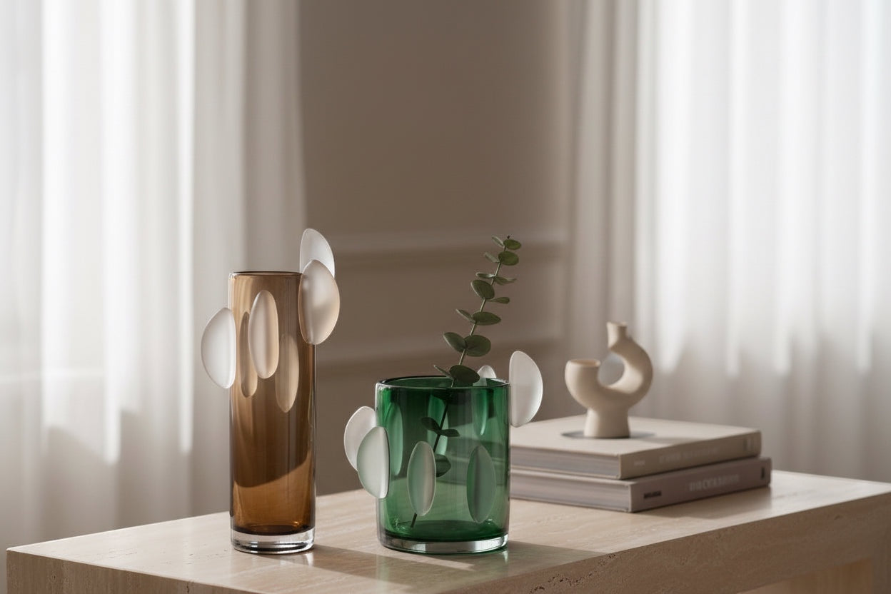 Eclectic amber brown and green glass disc vases on a wooden table with a sculptural ornament and books.