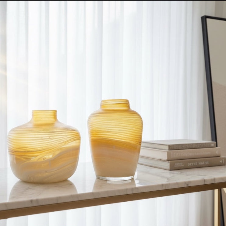 Eclectic amber marble effect glass vases with horizontal texture on a white marble console table.