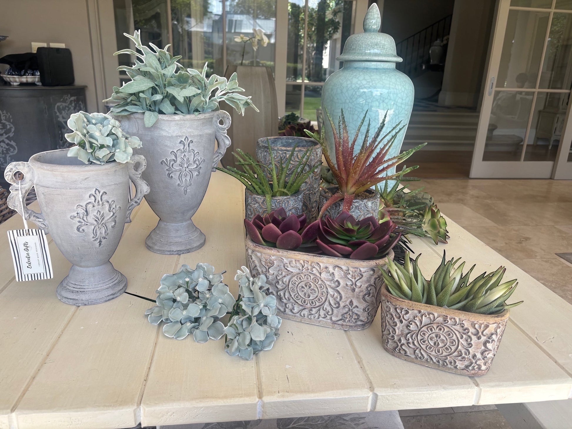 Eclectic antique cement trophy vase planters with ornate handles and weathered finish displayed on a table with plants