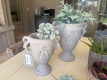 Eclectic antique cement trophy vase planter with ornate handles and weathered finish on a wooden table