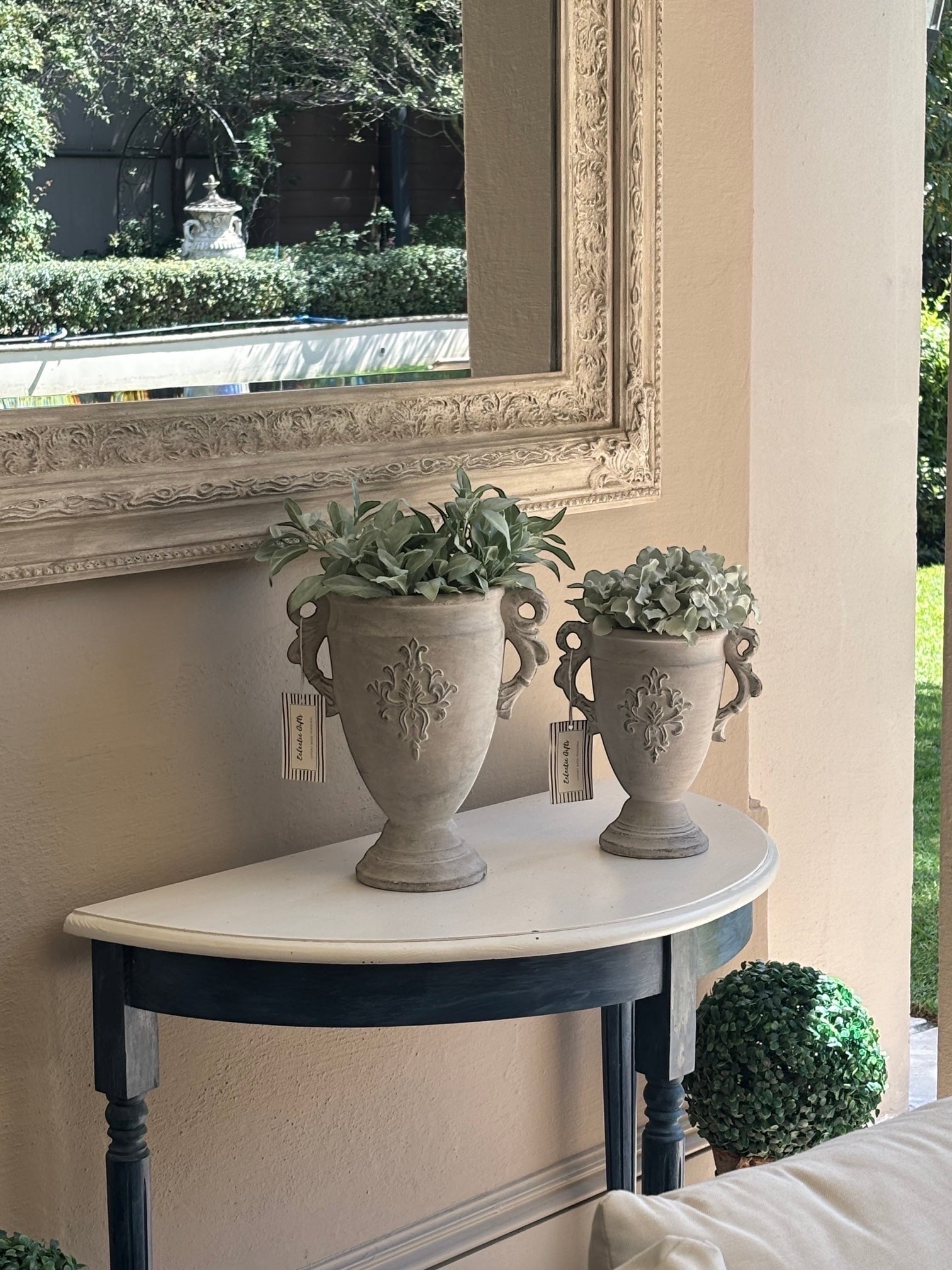 Eclectic antique cement trophy vase planters with ornate handles and weathered finish on a console table