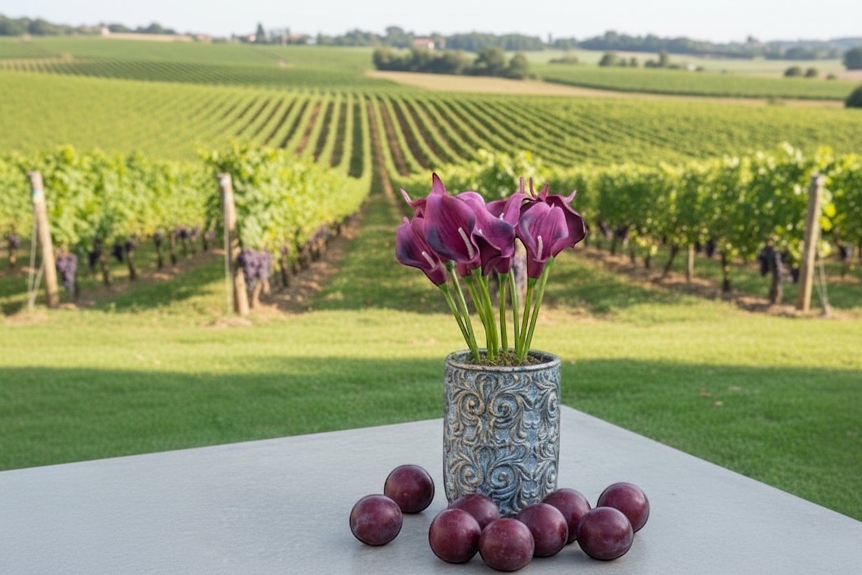 Eclectic antique scroll cement planter with aged green patina holding purple calla lilies on a table in a vineyard.