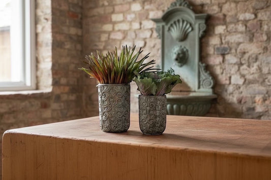 Eclectic antique scroll cement planters in green-grey with bronze undertones, styled with succulents on a wooden table.