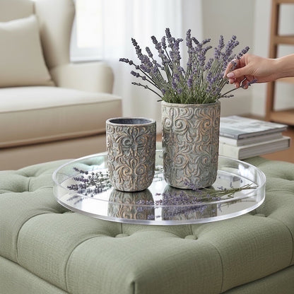 Eclectic antique scroll cement planters in green and bronze with lavender on a mirrored tray atop a tufted ottoman.