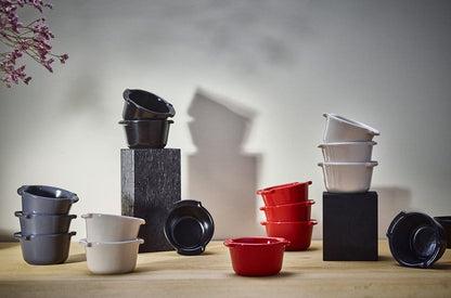 Eclectic collection of Appolia ceramic ramekins in black, red, grey, and white arranged on a wooden table.
