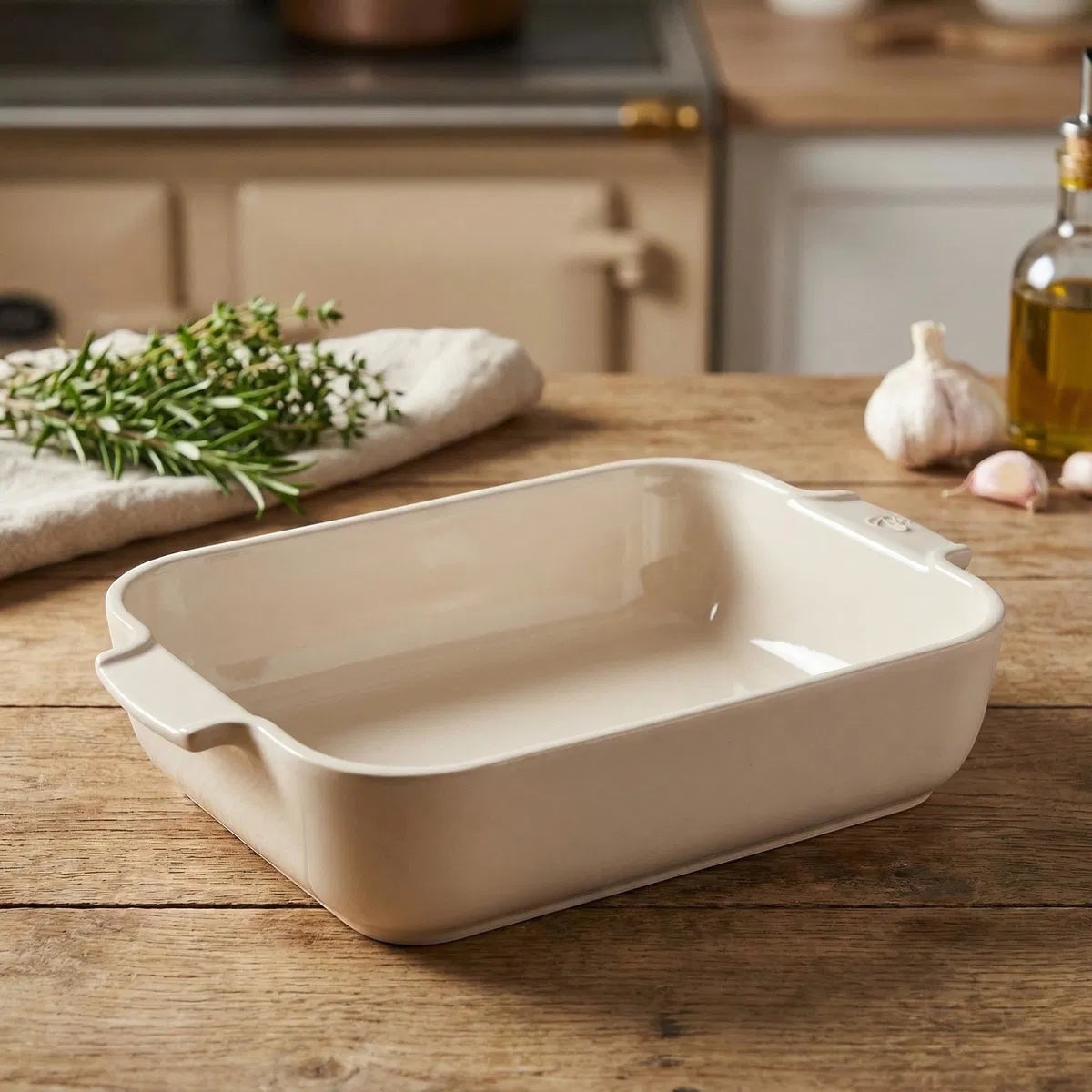Eclectic Appolia rectangular ceramic oven dish in a soft ecru glaze with wide ribbed handles on a wooden kitchen table.