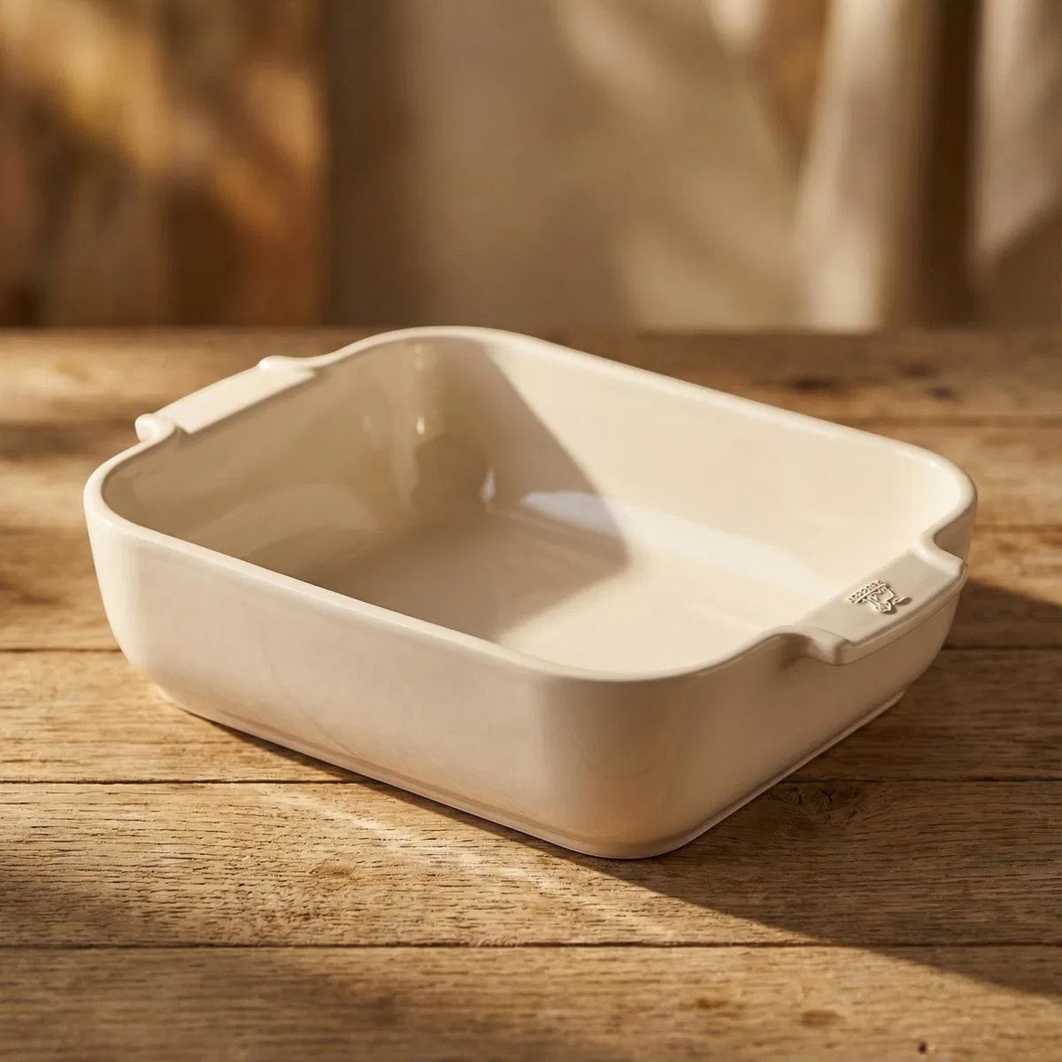 Eclectic Appolia rectangular ceramic oven dish in a soft ecru glaze with wide ribbed handles on a wooden table.