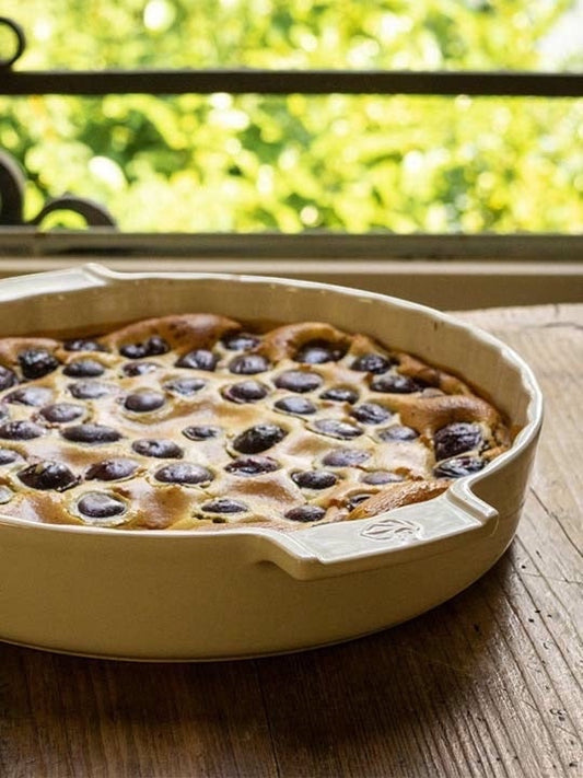 Eclectic Appolia 33 cm ecru ceramic pie dish filled with a baked cherry clafoutis on a rustic wooden table.