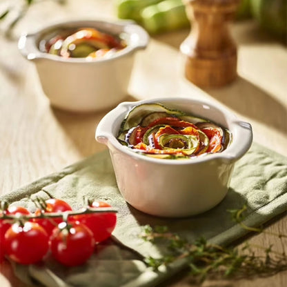 Eclectic Appolia ecru ceramic ramekins filled with baked vegetable tian on a wooden table with cherry tomatoes.