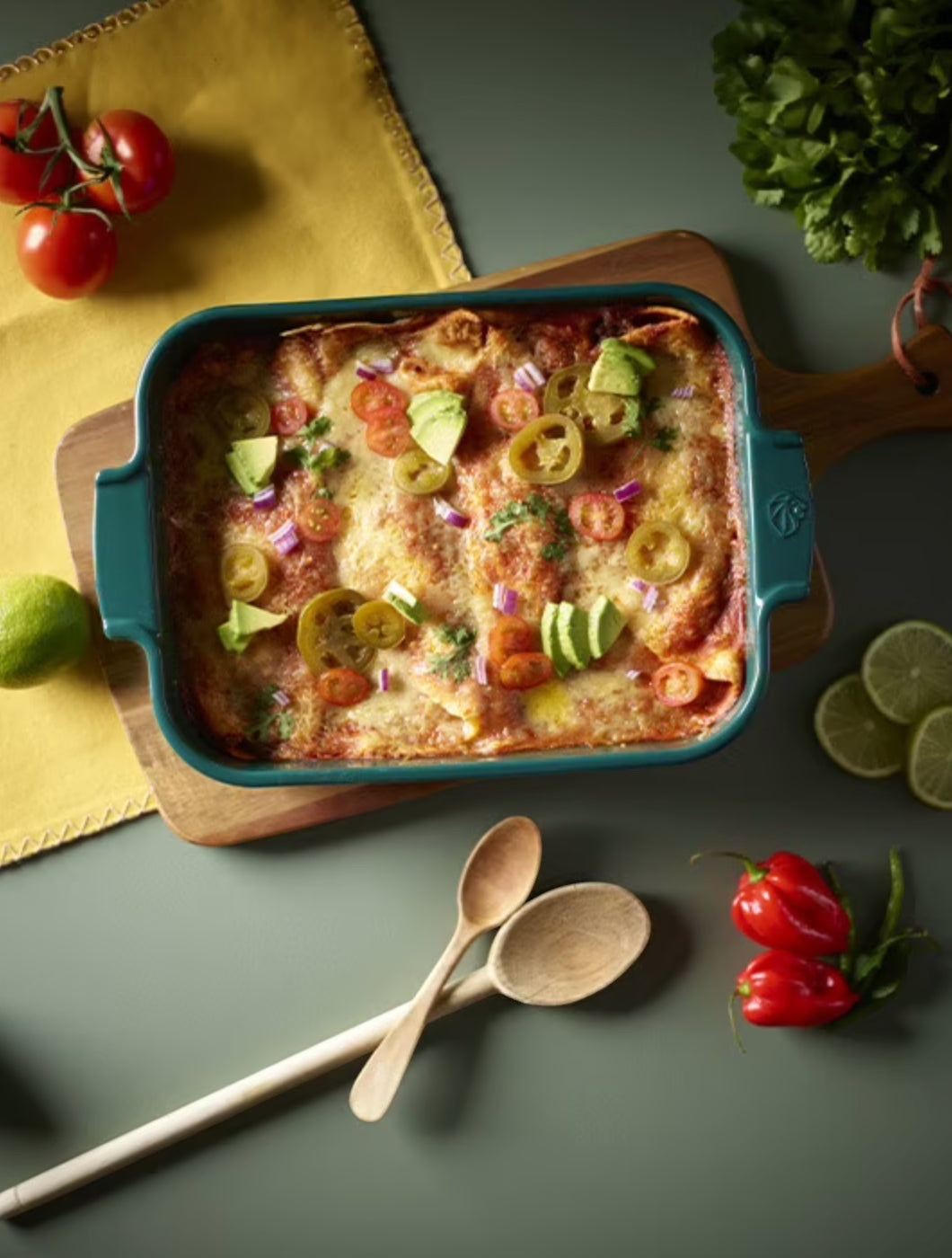 Eclectic Appolia forest green ceramic rectangular oven dish filled with baked enchiladas on a wooden serving board.