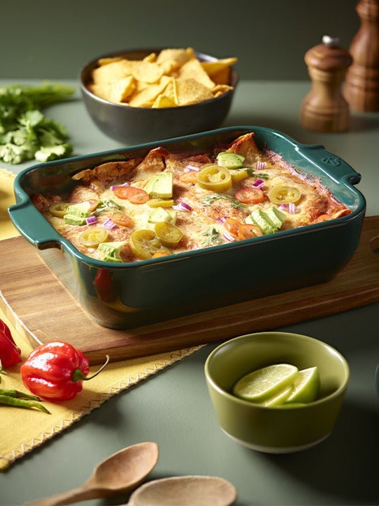 Eclectic Appolia forest green ceramic rectangular oven dish filled with baked enchiladas on a wooden serving board.